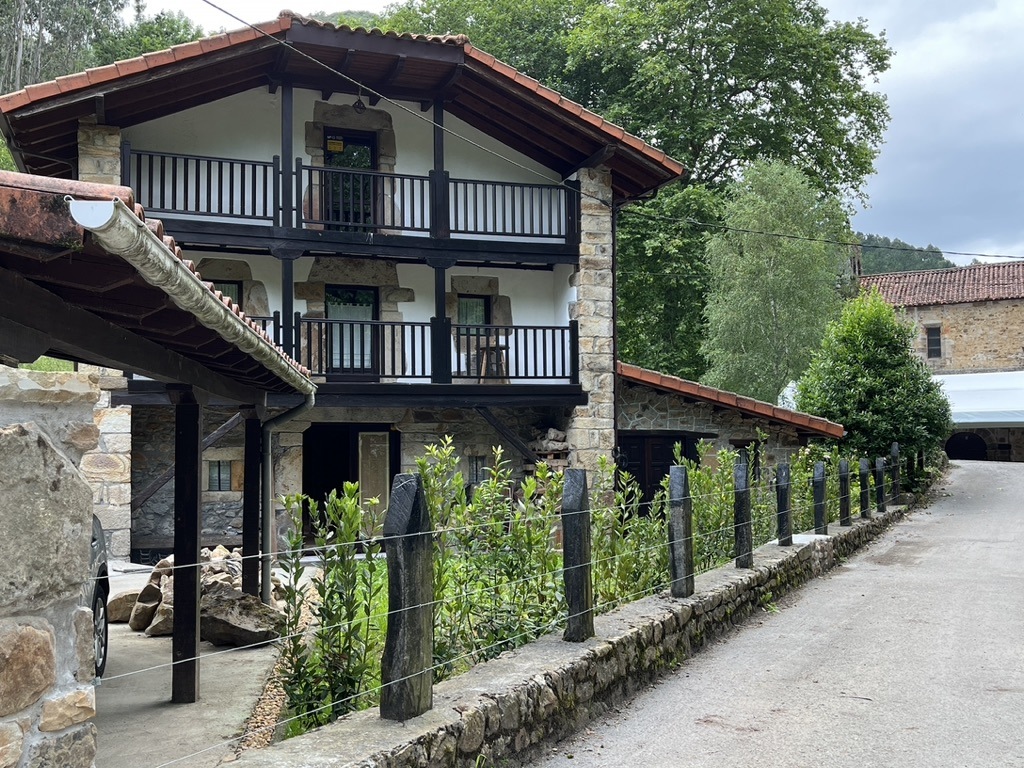 Jardín armónico junto a casa de piedra, con arbustos alineados y vallado de postes negros.