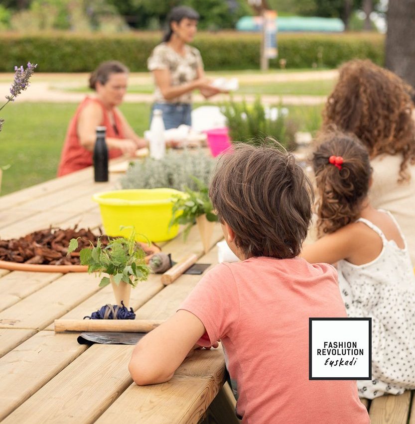 Niños y adultos en un taller de jardinería alrededor de una mesa de madera en un espacio verde.