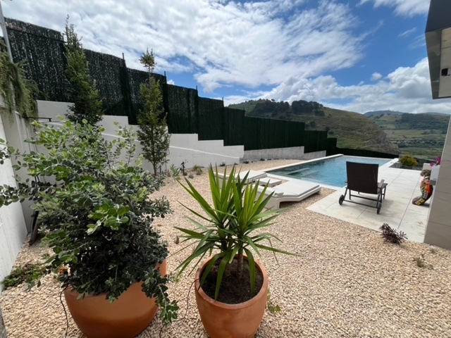 Jardín mediterráneo con grava, macetas de barro y piscina con tumbonas.
