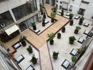 Patio interior con tarima de madera, maceteros y lucernarios en el suelo.