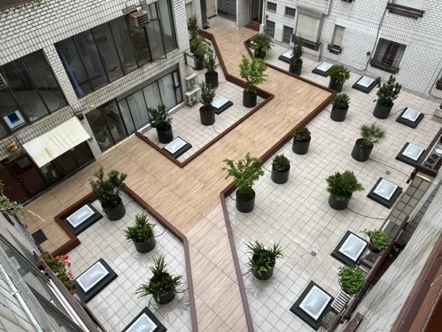 Patio interior con tarima de madera, maceteros y lucernarios en el suelo.