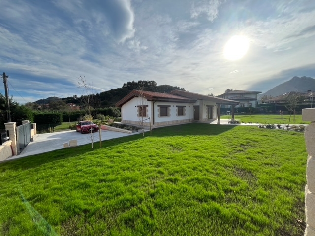 Plan de jardín con gran pradera de césped frente a una vivienda, con acceso y coche aparcado.